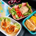 Colorful assortment of road trip snacks on a car seat including popcorn, nuts, and fruit.