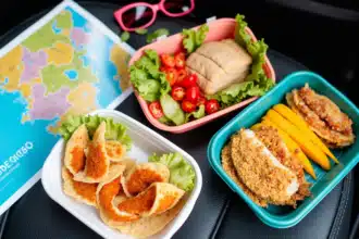 Colorful assortment of road trip snacks on a car seat including popcorn, nuts, and fruit.